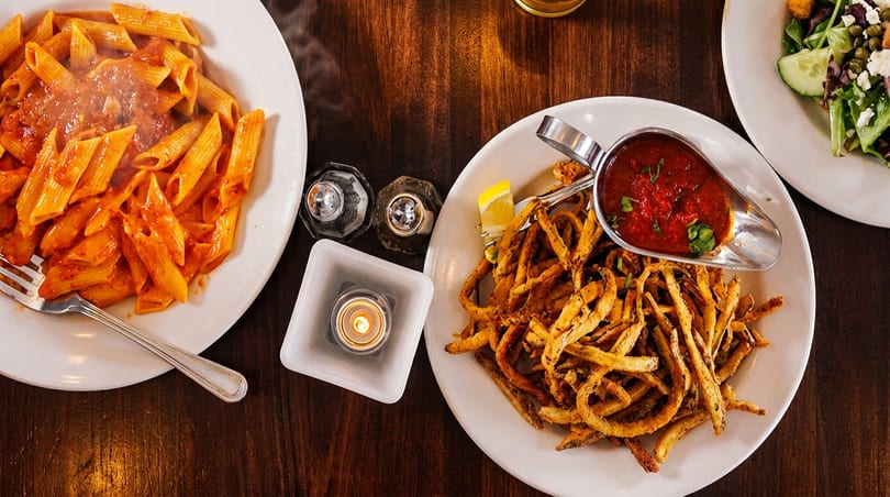 Overhead view of penne pasta, fried calamari with marinara, and a side salad on a wooden table.
