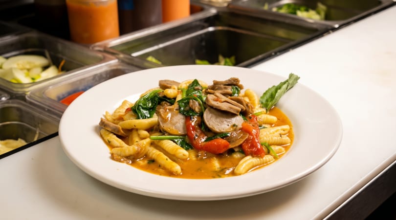 Plate of cavatelli pasta with sausage, spinach, and tomatoes in a savory sauce.