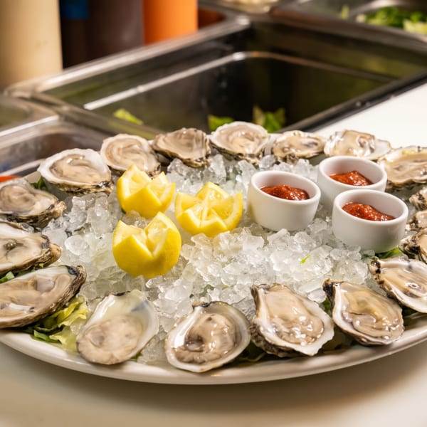Platter of fresh oysters on ice with lemon wedges and cocktail sauce cups.