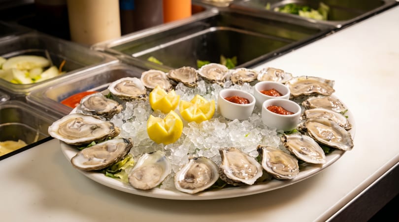 Platter of fresh oysters on ice with lemon wedges and cocktail sauce cups.