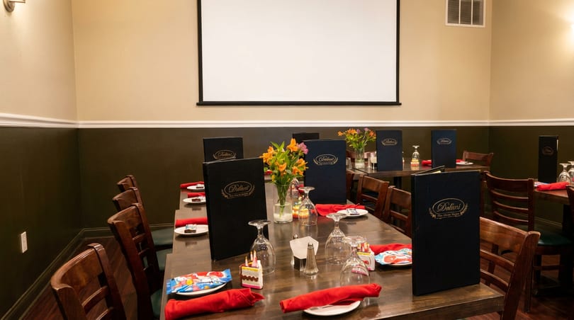 A private dining room at Doliani's with set tables, menus, and a projector screen.