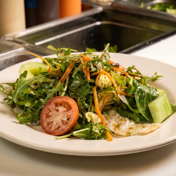 A fresh green salad with tomato, carrots, and cucumber on a white plate at a salad bar.