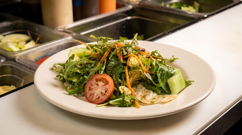 A fresh green salad with tomato, carrots, and cucumber on a white plate at a salad bar.