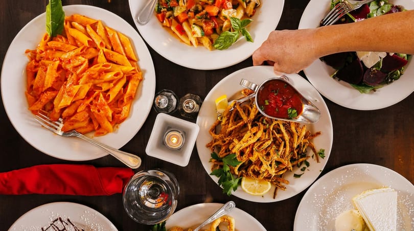 Overhead view of a table laden with Italian dishes, including pasta, fried calamari, and salad.
