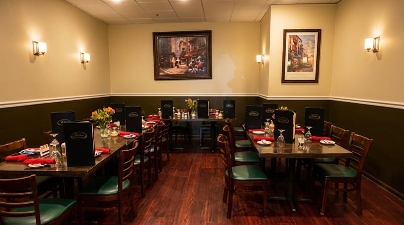 Dining room with set tables, dark green chairs, and paintings on light yellow walls.