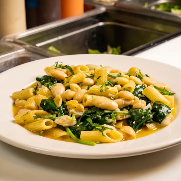 Rigatoni pasta with white beans and spinach in a light sauce on a white plate.